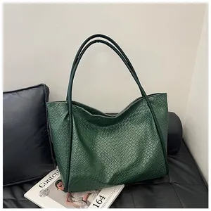Detail shot of a dark green crocodile pattern leather tote bag on a black sofa