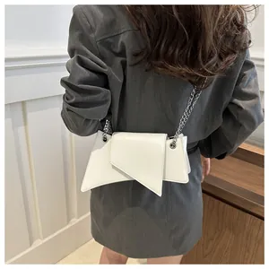 Detalle de bolso geométrico blanco con correa de cadena y solapa asimétrica sobre un vestido