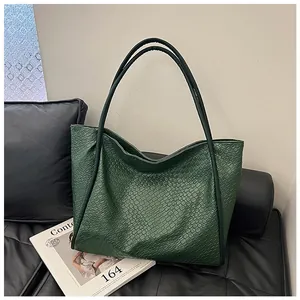 Detail shot of a dark green tote bag with embossed crocodile texture on a leather sofa