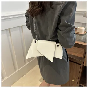 Detalle de bolso bandolera blanco asimétrico con cadena plateada llevado por una modelo
