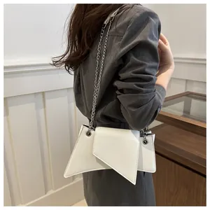 Bolso de hombro geométrico beige minimalista con cadena plateada llevado por la modelo
