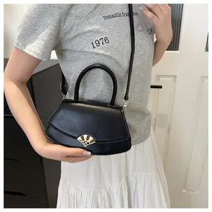 Détail d'un sac bandoulière chic en cuir noir avec boucle dorée en éventail sur un modèle