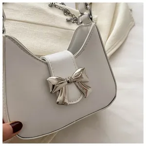 Détail macro du fermoir nœud en métal argenté sur un sac bandoulière en cuir blanc