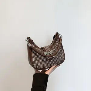 Dark brown underarm bag with silver studs and metal bow, shown held in hand