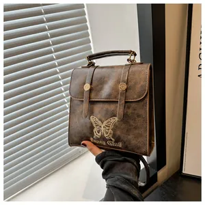 Close-up of brown textured leather bag featuring golden butterfly embroidery and metal buckles