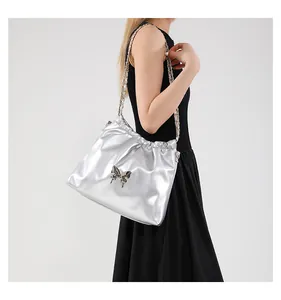 Detail of silver metallic bucket bag with chain strap and butterfly ornament on model