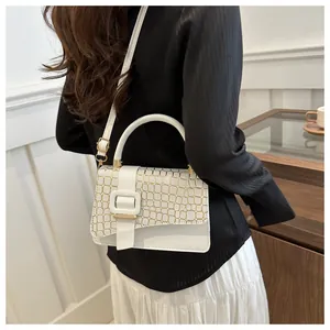 Detail of white square crossbody bag with gold crocodile texture and metal buckle flap