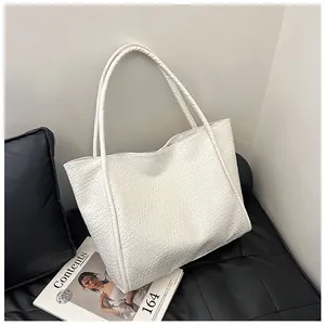Detailed view of white tote bag featuring snake-embossed faux leather texture on black sofa
