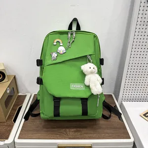 Détail d'un sac à dos scolaire vert avec étiquettes mode, épinglettes et un ours en peluche