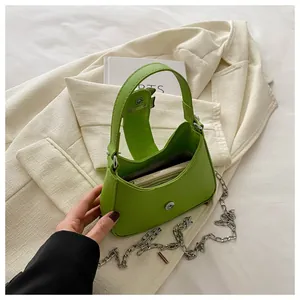 Détail d'un sac à main en cuir vert avec chaîne argentée sur un blazer beige