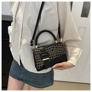 Close-up of black leather bag featuring golden geometric grid pattern and adjustable strap