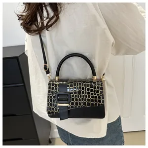 Detail of black crocodile texture small square bag with gold lines and metallic hardware