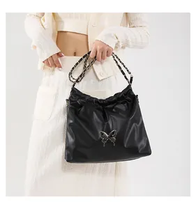 Détail d'un sac seau noir en PU avec design plissé et logo papillon en métal doré