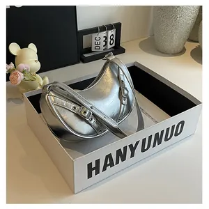 Detailed close-up of metallic silver crescent underarm bag with buckle strap on white box