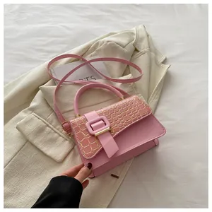 Close-up of pink shoulder bag with textured crocodile pattern and gold trim on white blazer