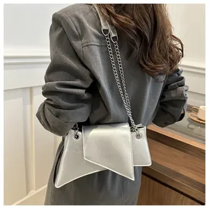 Detalle del bolso geométrico plateado con cadena de metal sobre un abrigo gris