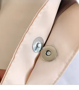 Detailed macro of the metallic magnetic clasp and silk lining of the pink nylon bag