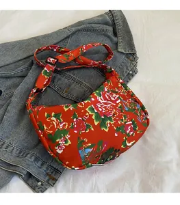 Dettaglio borsa a mezzaluna in nylon floreale con tracolla regolabile su denim blu