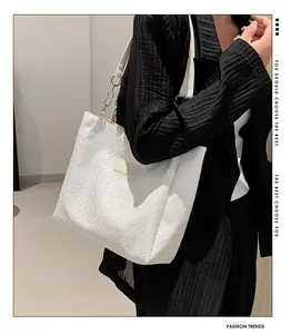 Detail of white woven tote bag with silver chain and fashion plate on black outfit