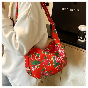 Dettaglio della borsa a mezzaluna in nylon a fiori rossi indossata con tracolla