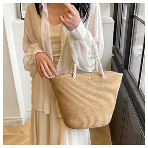 Détail de la texture tressée et des poignées en coton crème d'un sac cabas en paille