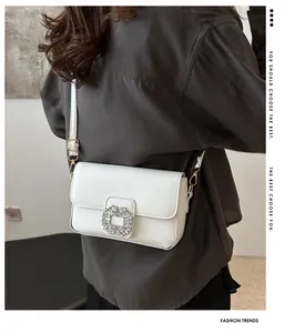 Detailed close-up of a white leather crossbody bag featuring a luxury square crystal buckle