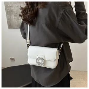 Close-up of a white leather crossbody bag with a sparkling crystal square buckle on model