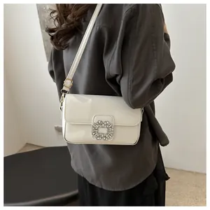 Detail of white patent leather shoulder bag with a square rhinestone buckle and gold buckle