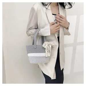 Detail of hand-woven straw bag with grey white stripes and cream lace bow charm