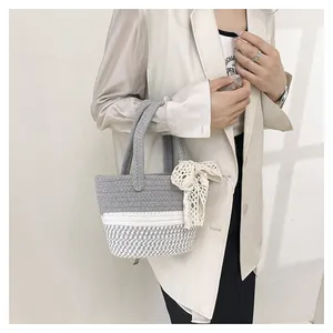 Detail of gray woven cotton bucket bag featuring a white lace bow and rope texture
