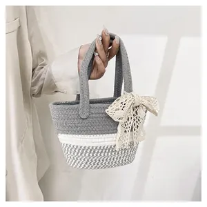 Close-up of hand-woven cotton straw bag featuring grey contrast and beige lace bow detail