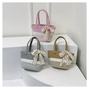 Three colorful woven tote bags with lace bows displayed on geometric white stands