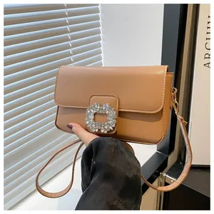 Close-up of a brown leather small square bag featuring a sparkling rhinestone buckle and gold hook