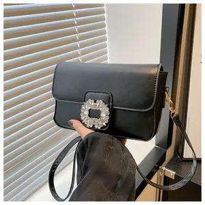 Detail of black crossbody bag featuring a sparkling rhinestone buckle and slim leather strap