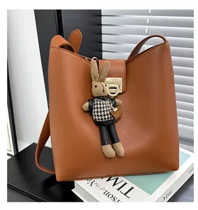 Détail d'un sac seau en PU marron avec boucle dorée et pendentif lapin en tricot sur livre