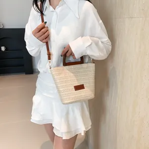 Detalle del bolso tipo cubo de paja beige con textura trenzada y asa de madera oscura