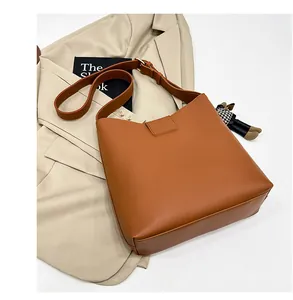 Détail du sac seau marron en similicuir avec bandoulière et pendentif sur blazer beige