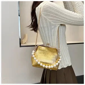 Detail of gold pleated shell bag with pearl handle and metallic chain strap for women