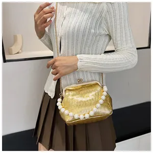 Detailed view of golden pleated shell bag with large pearl handle and metal chain strap