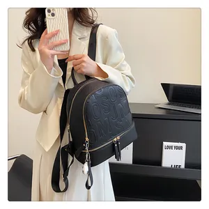 Detail of black pebbled leather backpack with embossed letters and gold metal zippers