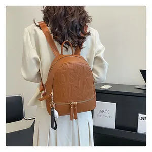 Detail of brown faux leather backpack featuring 3D embossed letters and metal zippers
