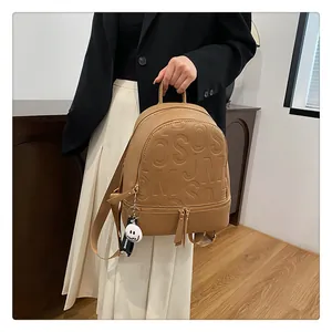Detail of a brown leather backpack with embossed letters and a smiling pendant on a model