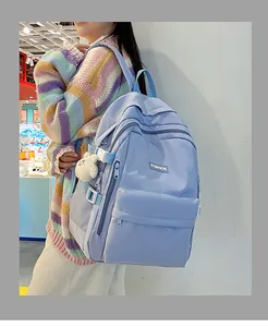 Detail of light blue nylon backpack with multiple zippers and white bear plush charm