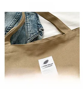 Détail d'un sac cabas en toile kaki avec une étiquette tissée blanche et un logo plume