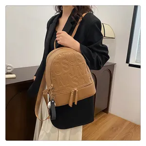 Detail of brown faux leather backpack featuring 3D letter embossing and gold dual zippers
