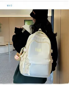 Rear view of a minimalist white nylon backpack showing side buckles and plush doll pendant