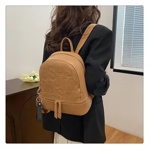 Detail of tan brown lychee texture backpack with large embossed letters and gold hardware
