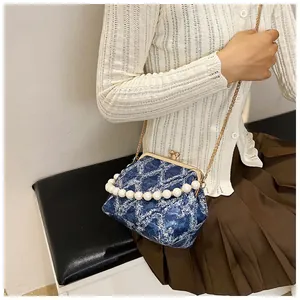 Quilted blue denim shell bag with pearl handle and gold chain worn by a model