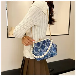 Detail view of denim shell bag with pearl handle and gold chain on model
