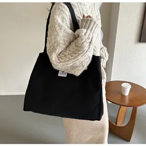 Détail d'un grand sac cabas en toile noire porté avec un pull en maille minimaliste